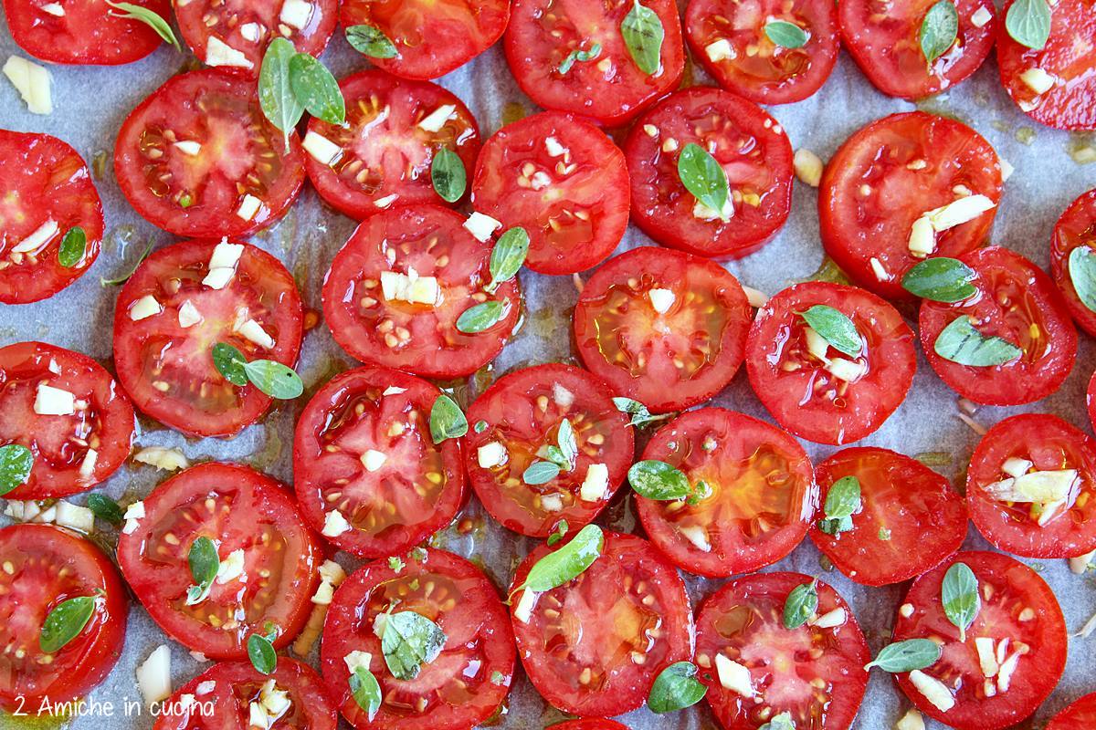 pomopdori datterini tagliati e conditi con olio, sale, aglio e maggiorana, pronti per essere infornati