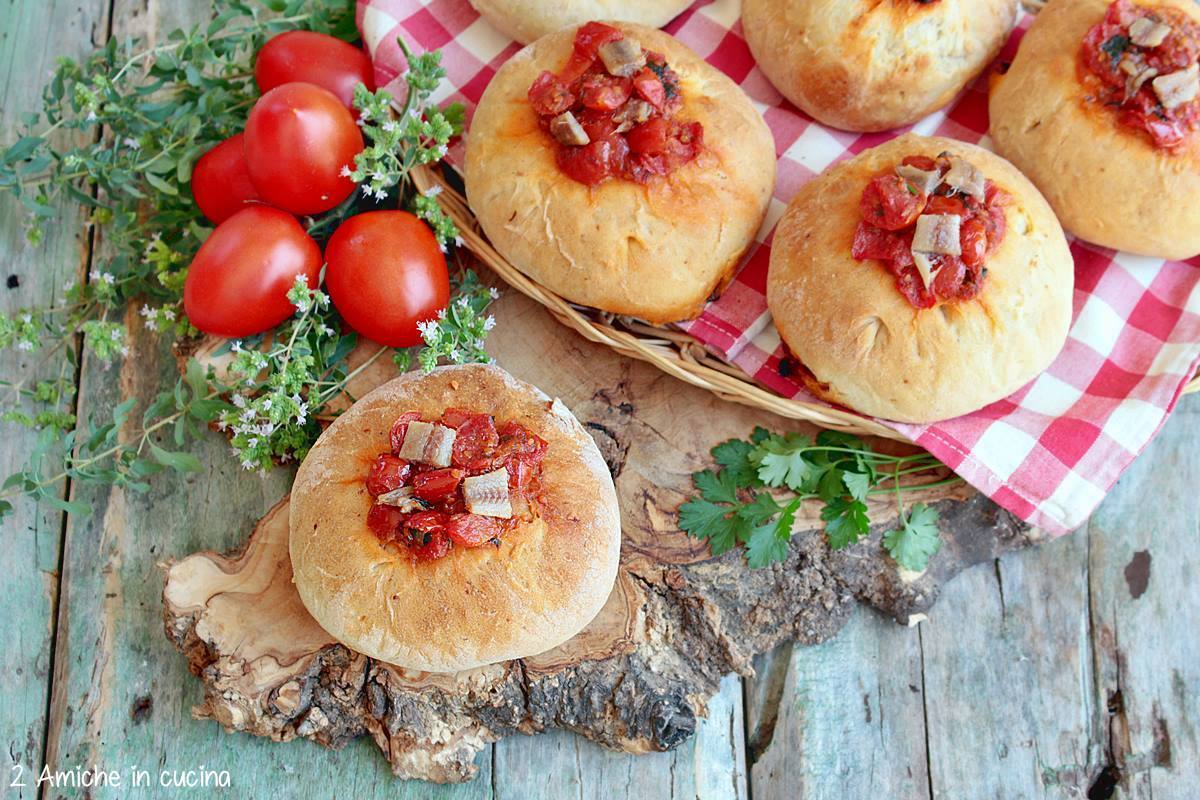 tagliere con pagnottelle ricoperte di pomodoro e alici