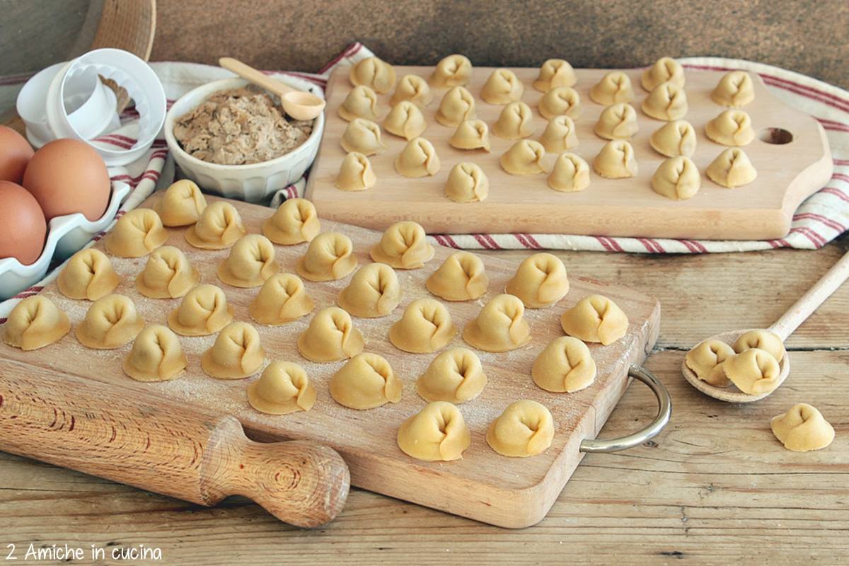 tagliere con cappelletti, mattarello e ciotola con ripieno di carne