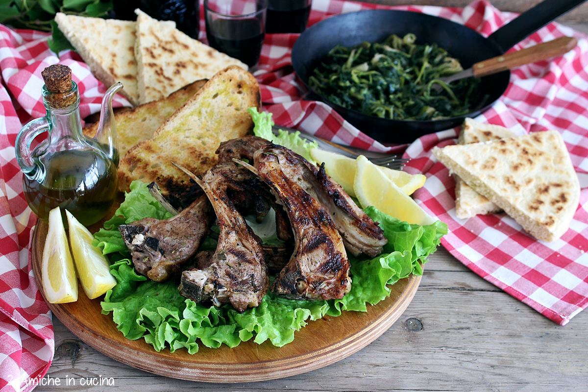 tagliere con costolette di agnello alla griglia, bruschetta, erbe di campo e torta al testo